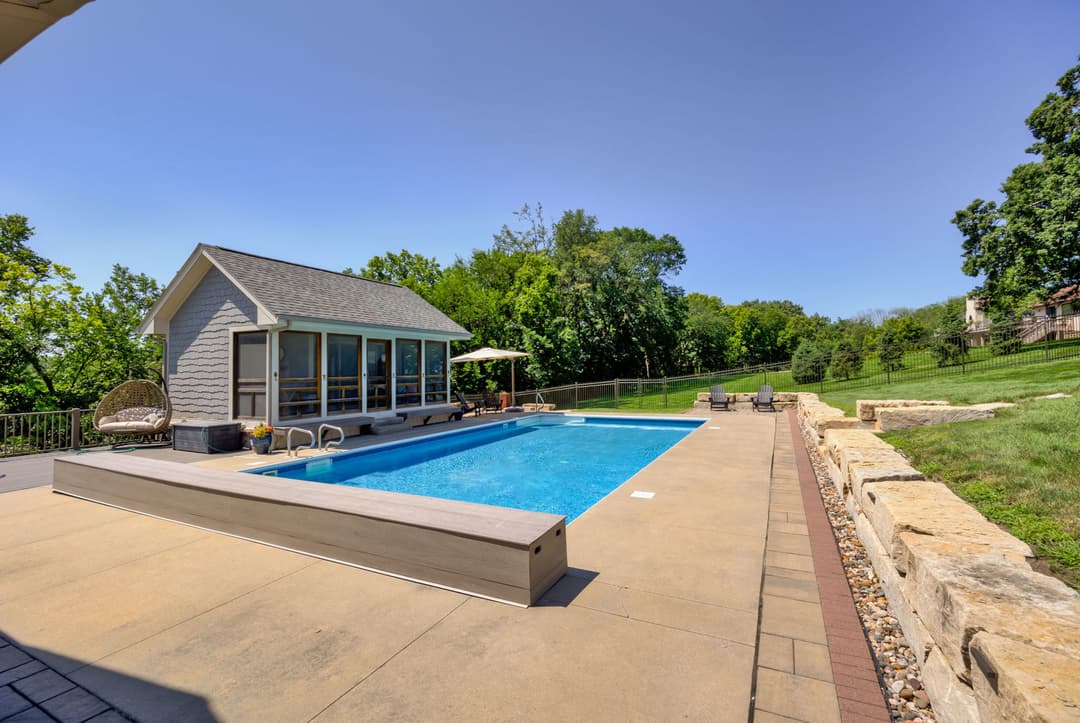 Modern backyard pool with lounge area and scenic green landscape under clear blue sky.
