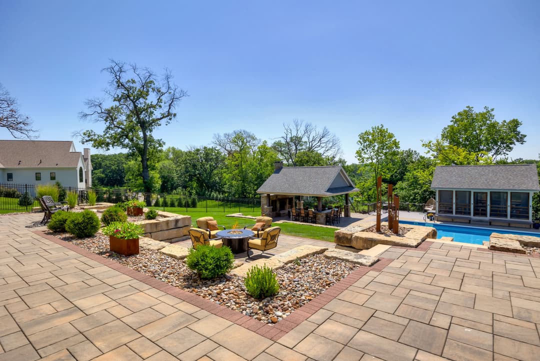 Spacious outdoor patio with lounge chairs, stone landscaping, and a poolside view.