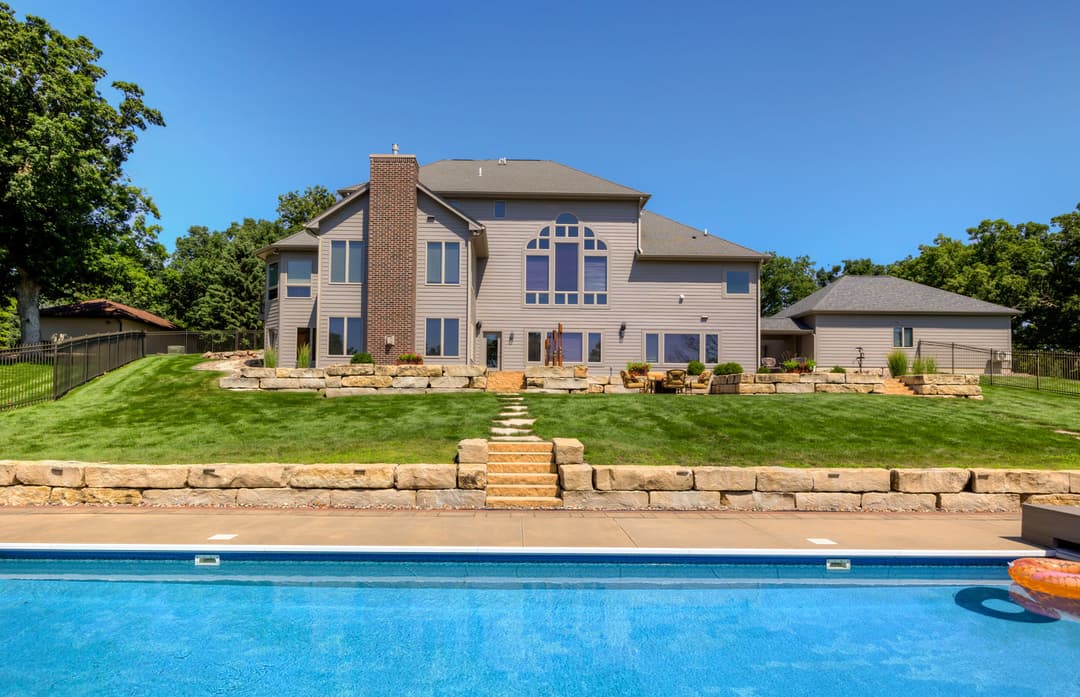 Luxury home with large windows, stone landscaping, and a pool in a sunny outdoor setting.