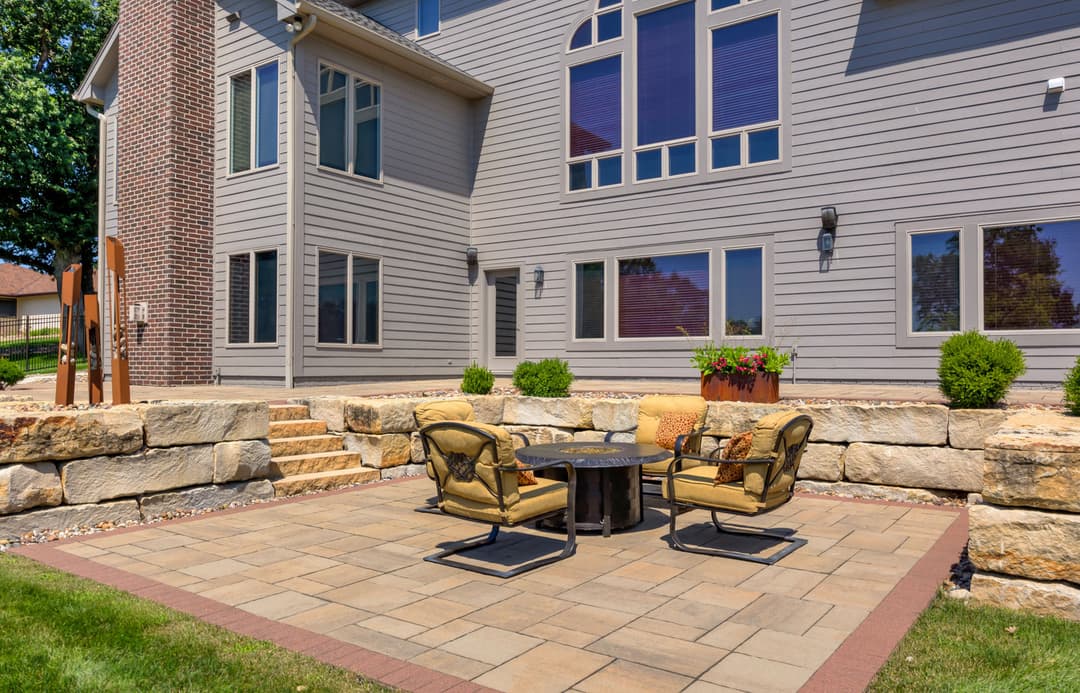 Cozy outdoor patio with seating and fire pit beside a modern home in a landscaped yard.