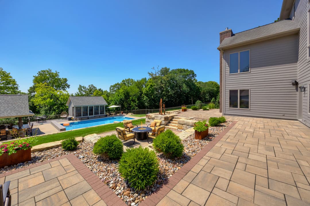 Backyard oasis featuring a pool, stone patio, seating area, and landscaped garden.