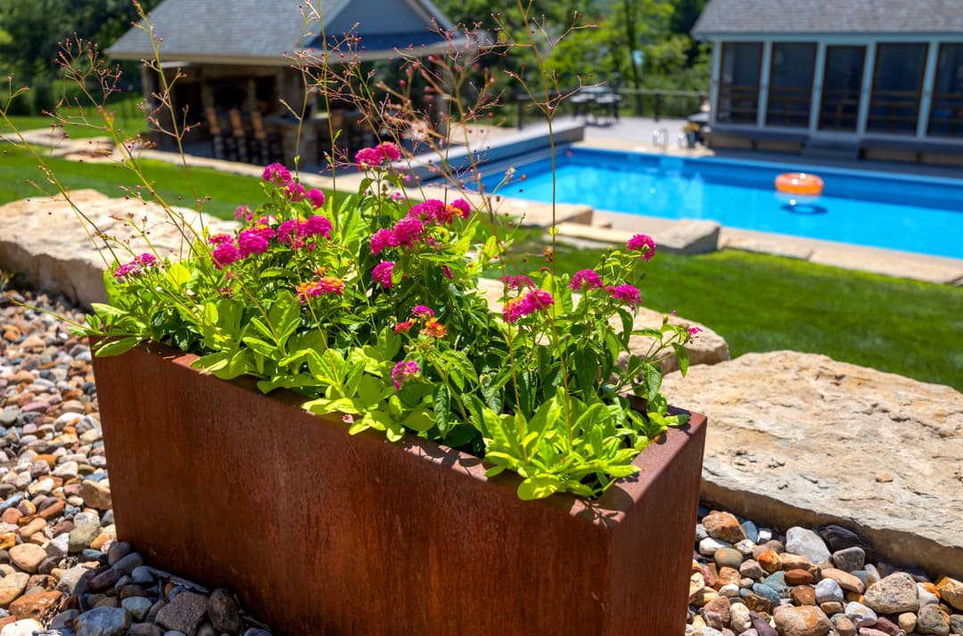 Vibrant pink flowers in a rust-colored planter near a pool and outdoor seating area.