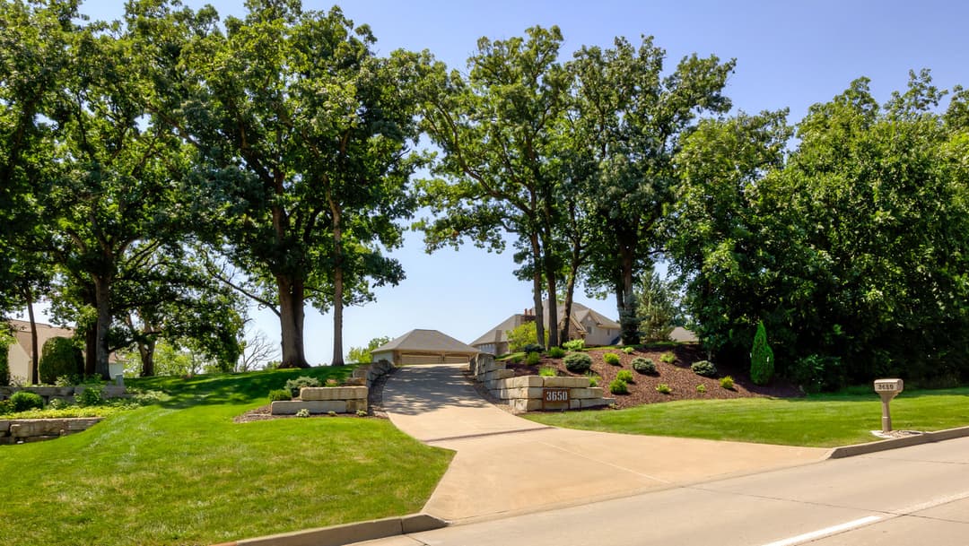 Residential driveway surrounded by trees and landscaped greenery in sunny weather.