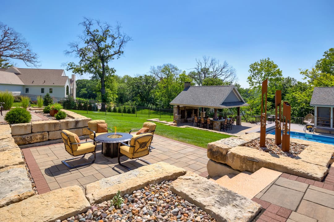 Outdoor patio with seating, fire pit, and pool area surrounded by lush greenery.