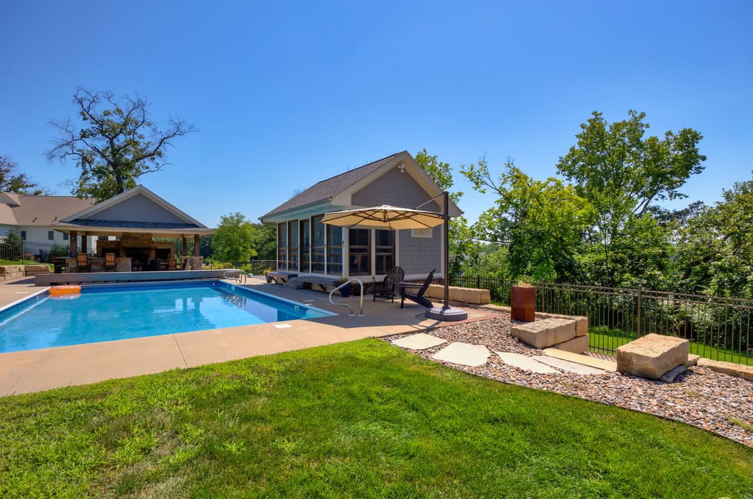 Modern backyard with swimming pool, patio, and lush greenery under a clear blue sky.
