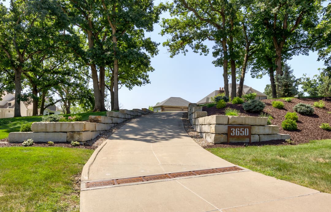 Elegant stone-lined driveway leading to a residential home with lush greenery and trees.