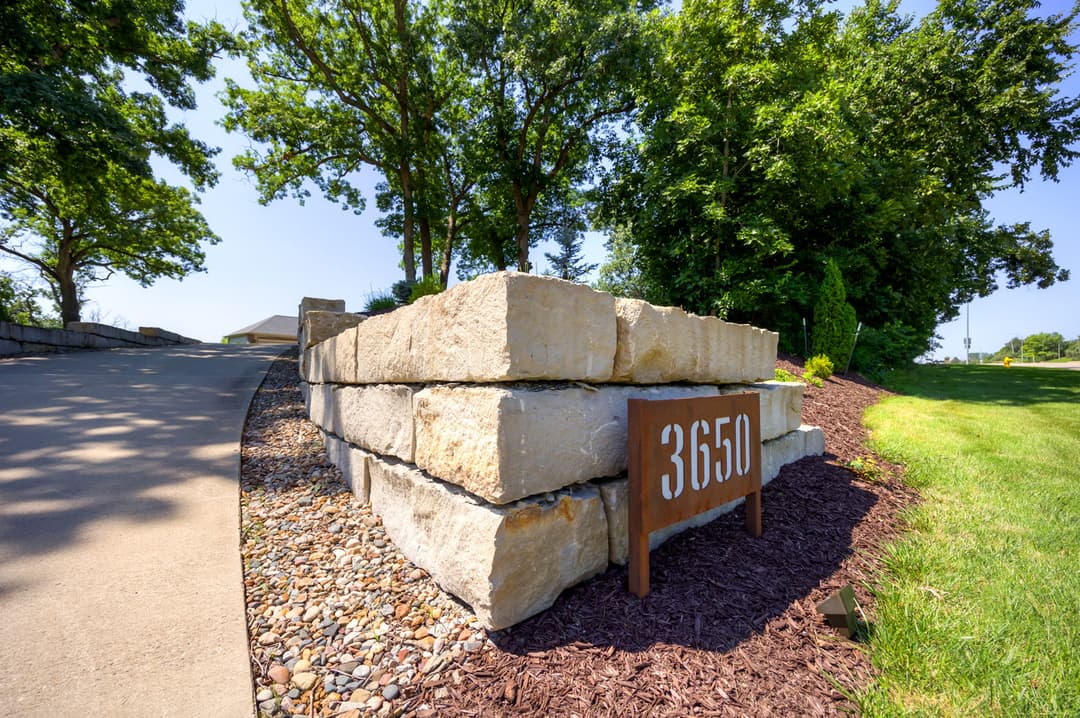 Address sign 3650 on a stone wall beside a landscaped driveway under clear blue skies.