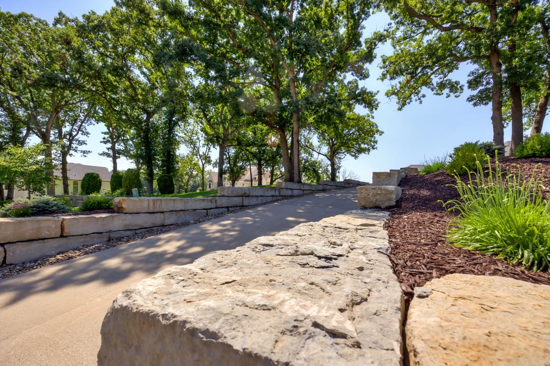Scenic pathway lined with stone and greenery, leading through trees on a sunny day.
