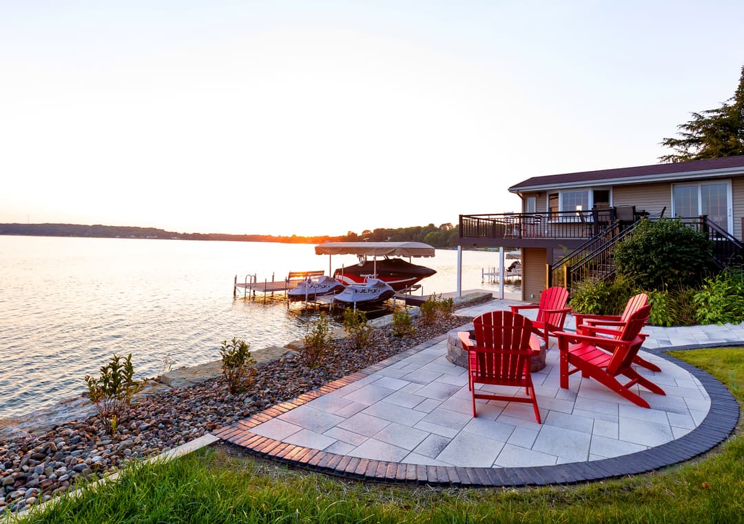 Red adirondack chairs by the lake at sunset, with boats docked nearby and a charming home.