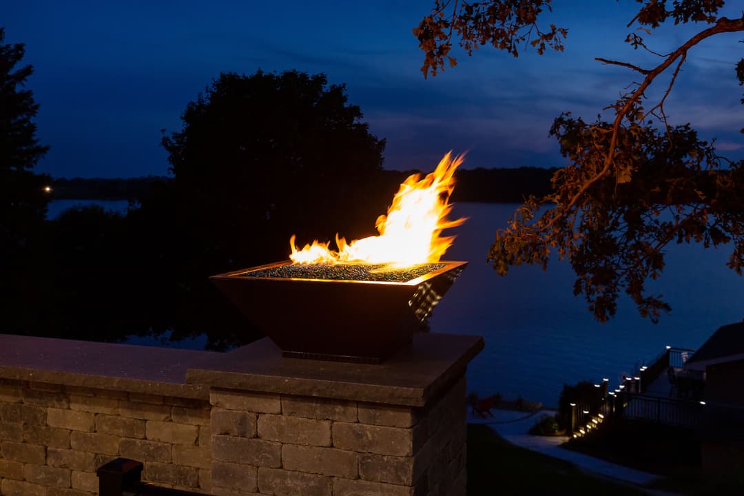 Stylish outdoor fire pit with vibrant flames overlooking a serene lake at dusk.