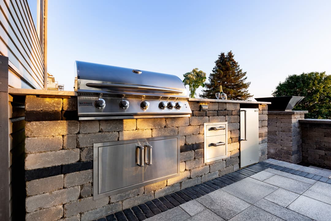Modern outdoor kitchen with a stainless steel grill, stone countertops, and storage cabinets.