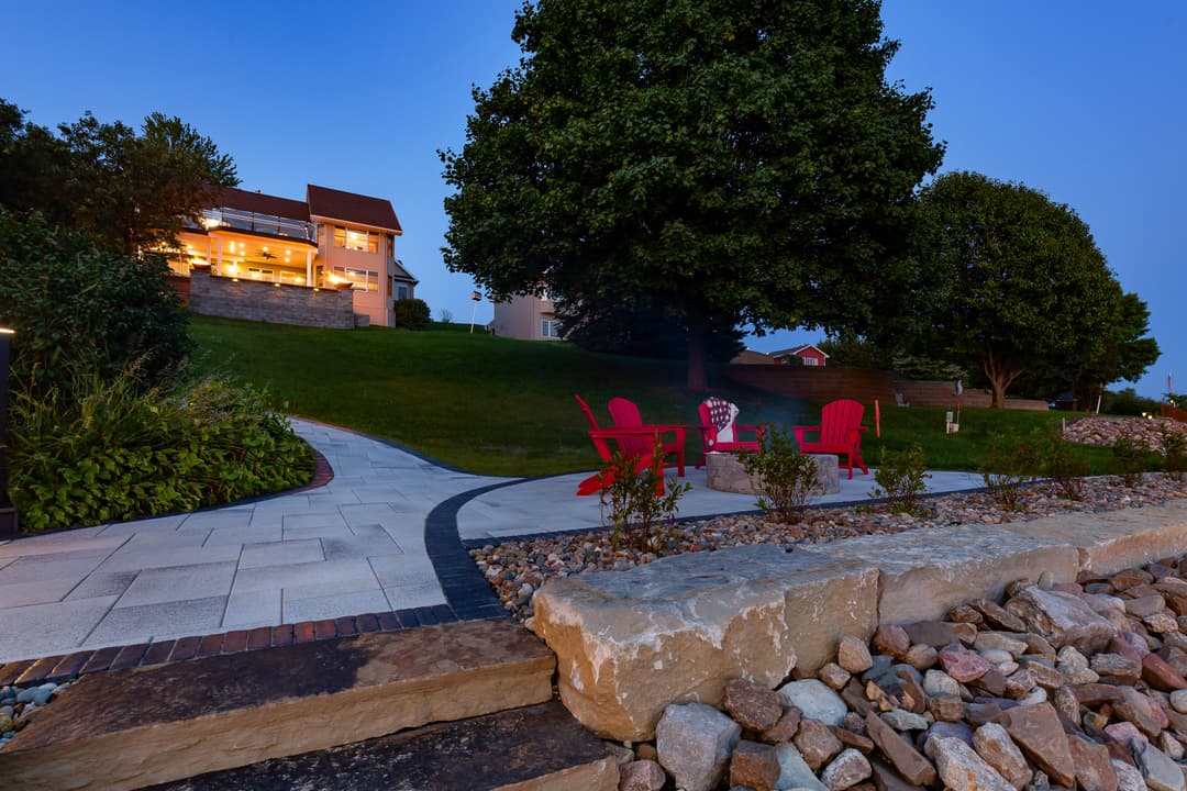Cozy backyard scene with red chairs, stone pathway, and a well-lit house at dusk.