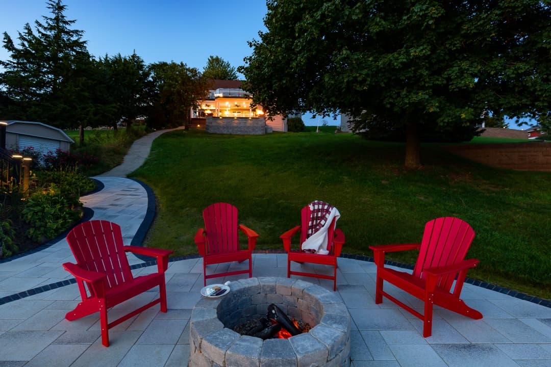 Cozy outdoor seating with red Adirondack chairs around a fire pit in a landscaped backyard.