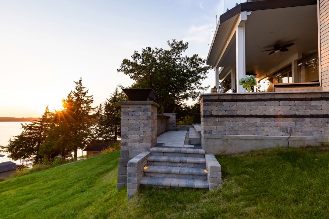 Sunset view of a stone staircase leading to a modern lakeside home surrounded by trees.