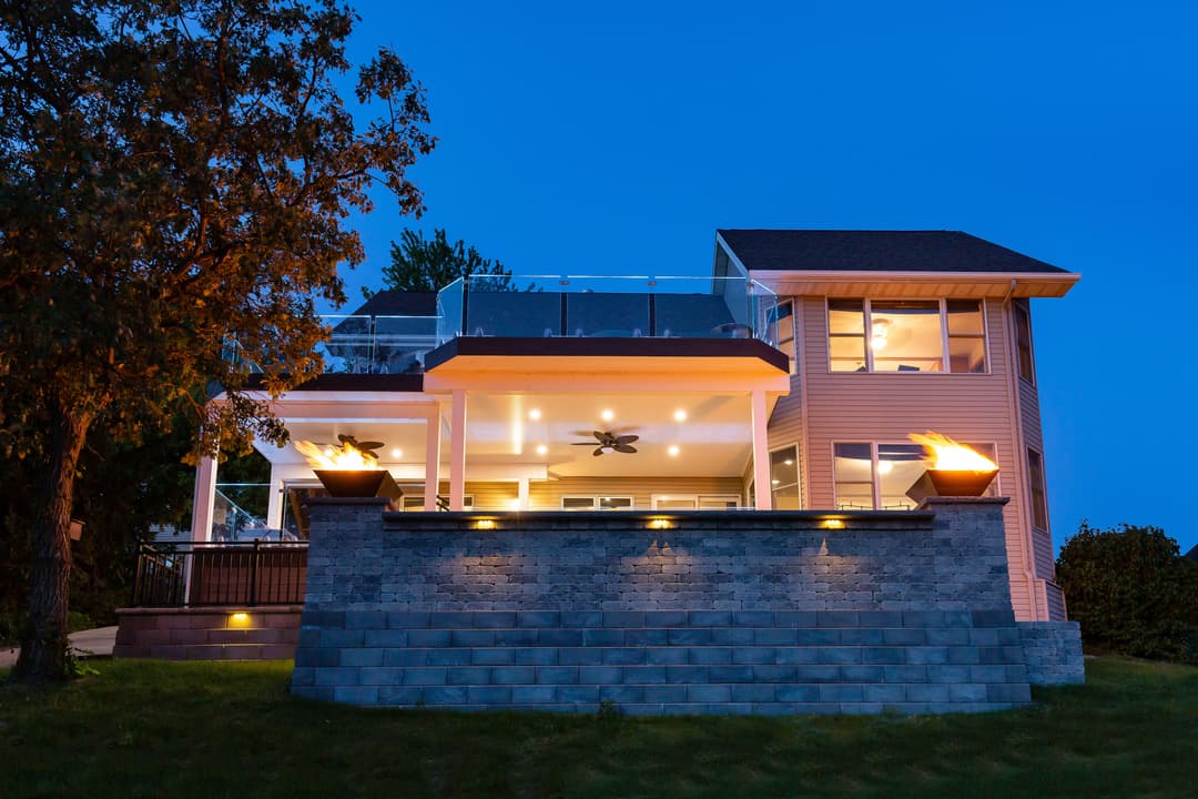 Modern lakefront house with illuminated outdoor patio and contemporary design at dusk.
