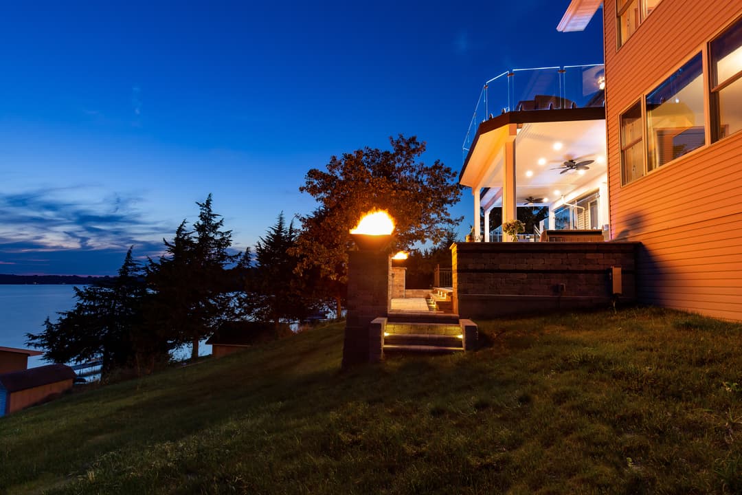 Modern lakeside home at dusk with outdoor fire feature and scenic views.