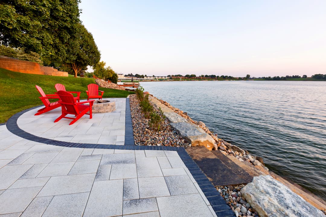 Scenic lakeside patio with red chairs, stone landscaping, and tranquil water views.