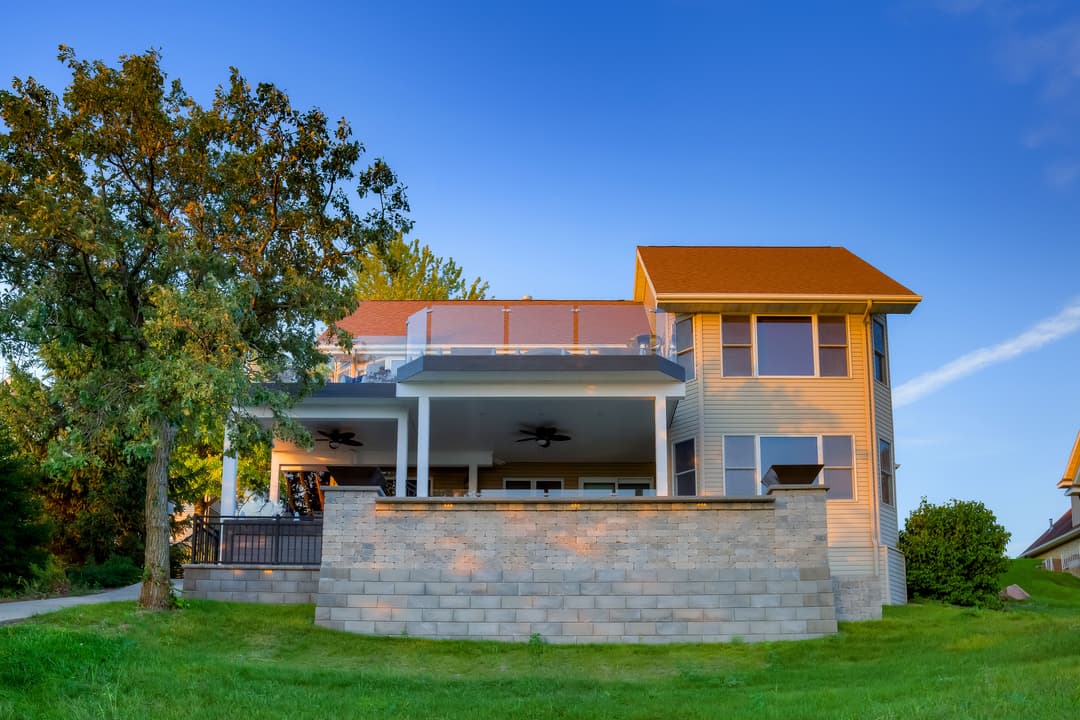 Modern two-story house with a spacious terrace and green lawn under a clear blue sky.
