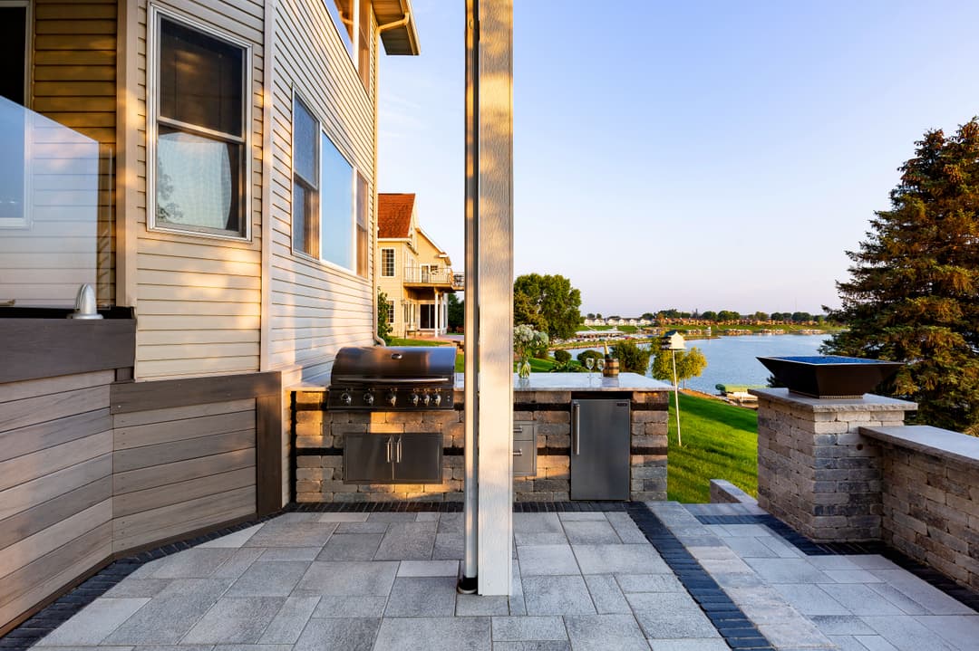 Modern outdoor patio with a grill, overlooking a serene lake at sunset.