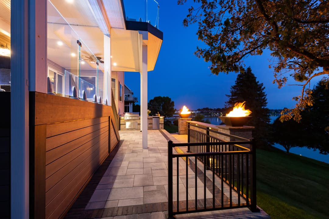 Elegant outdoor patio with fire bowls, lake view, and modern lighting at dusk.