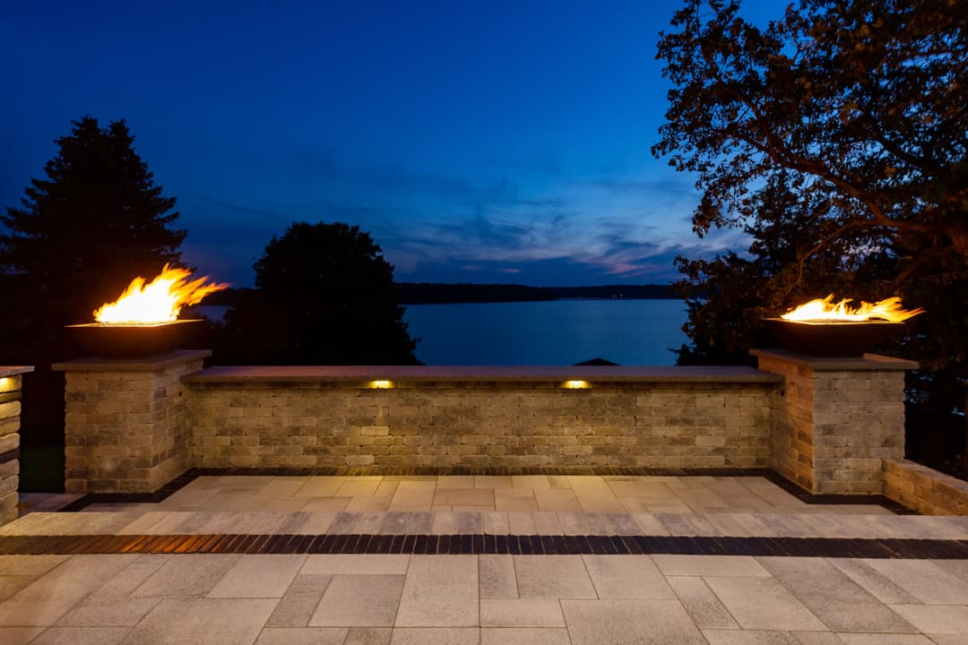 Modern patio with fire features overlooking a serene lakeside view at twilight.