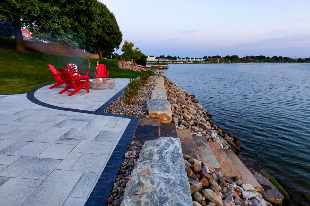 Scenic lakeside patio with red Adirondack chairs and stone walkway at sunset.
