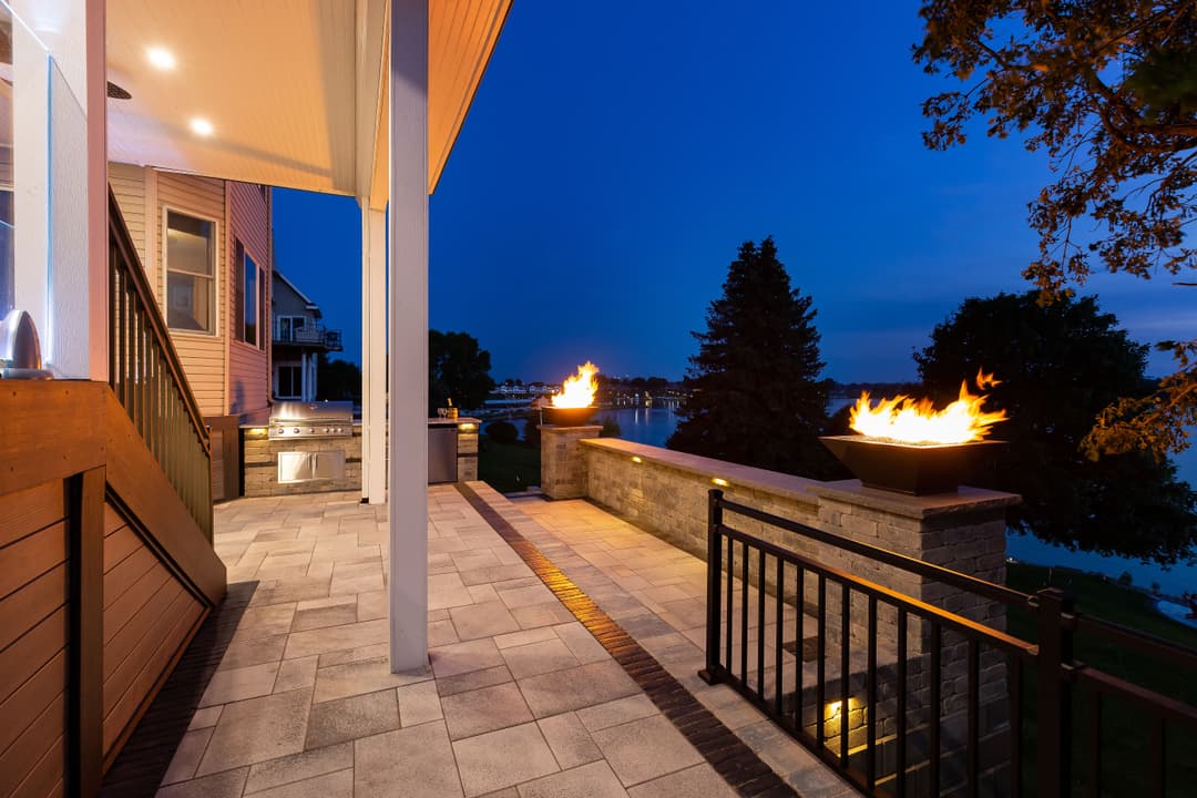 Modern lakeside patio with fire pits, outdoor kitchen, and twilight ambiance.