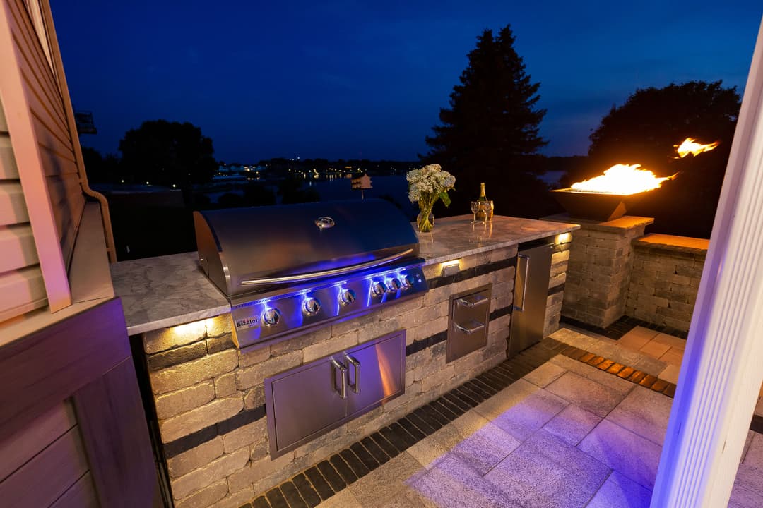 Modern outdoor kitchen with stainless steel grill and stone countertops, illuminated at night.