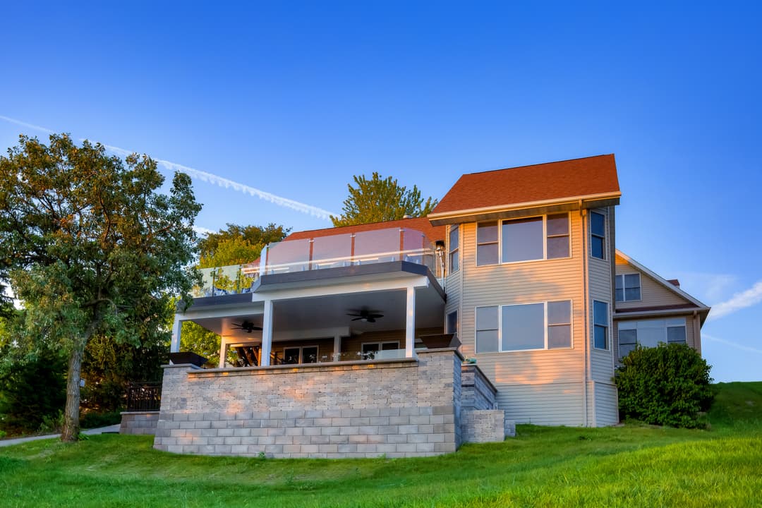 Modern two-story home with a large deck, overlooking a green lawn and blue sky.