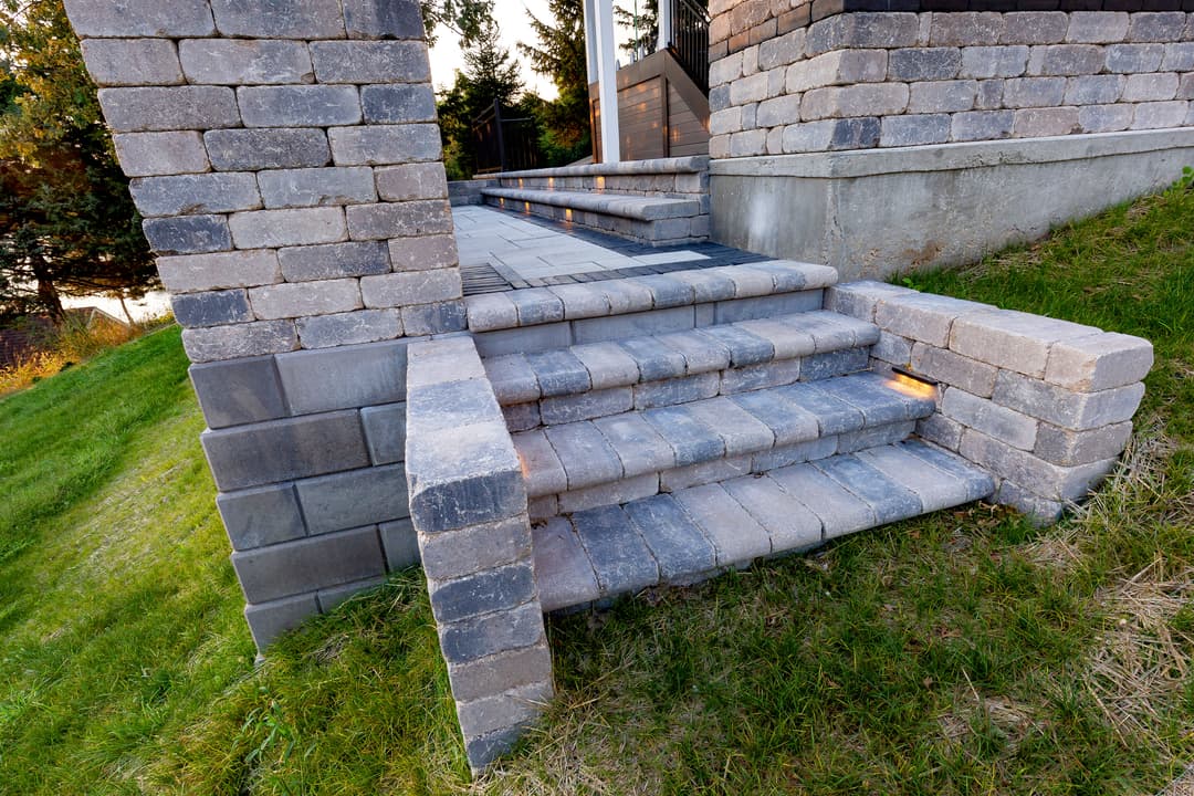 Stone step pathway leading to a landscaped area, featuring textured gray pavers and greenery.