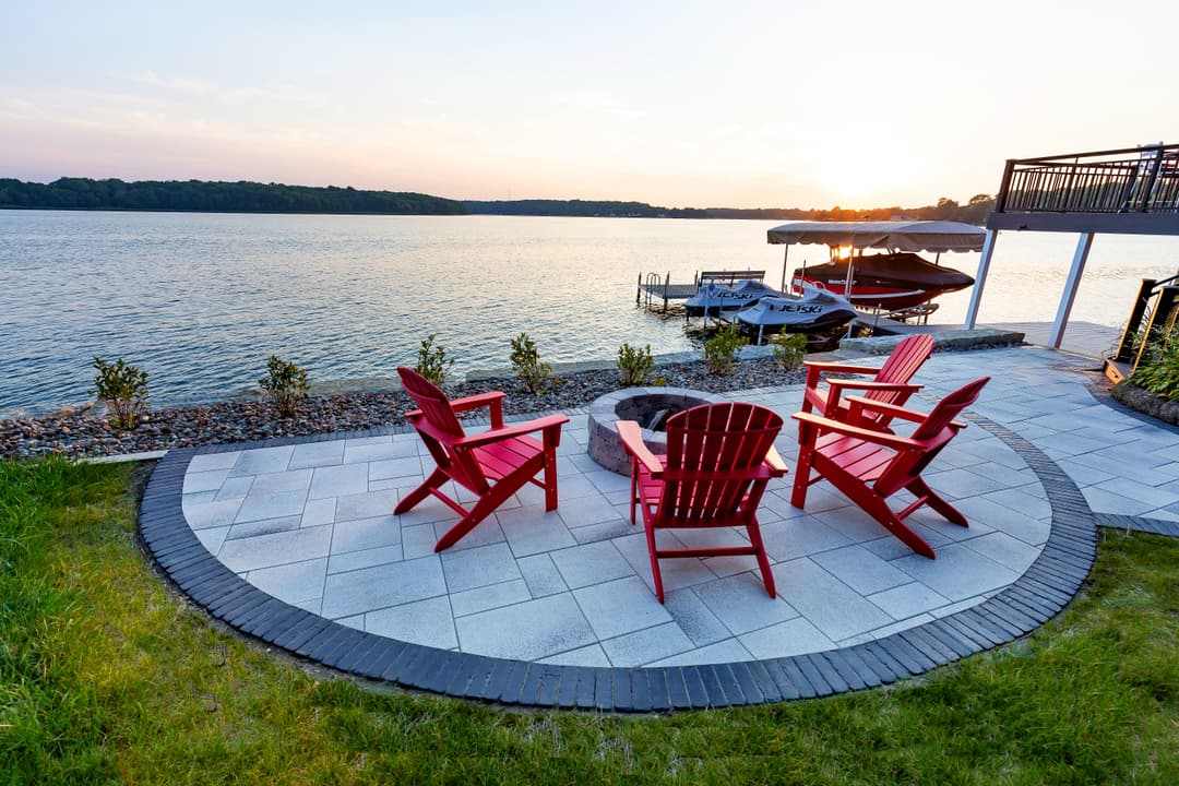 Scenic lakeside patio with red Adirondack chairs and fire pit at sunset.