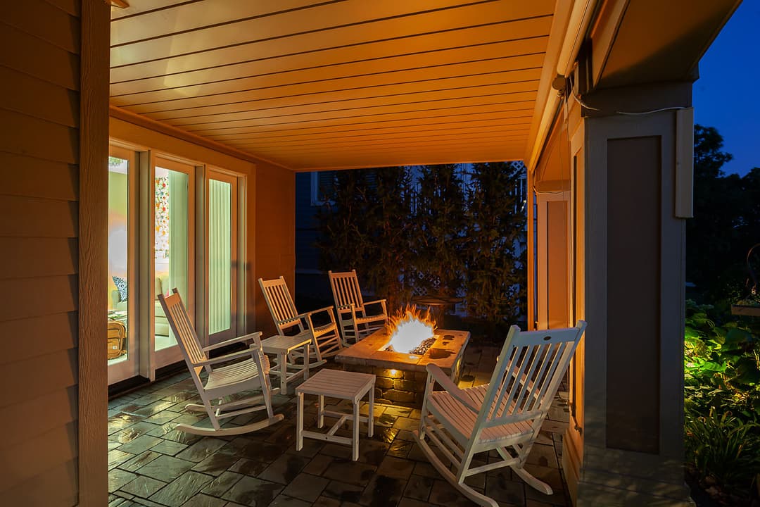 Cozy outdoor seating area with rocking chairs and a fire pit, illuminated at dusk.