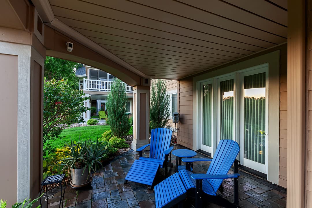 Cozy patio with blue lounge chairs, stone flooring, and lush greenery in the background.