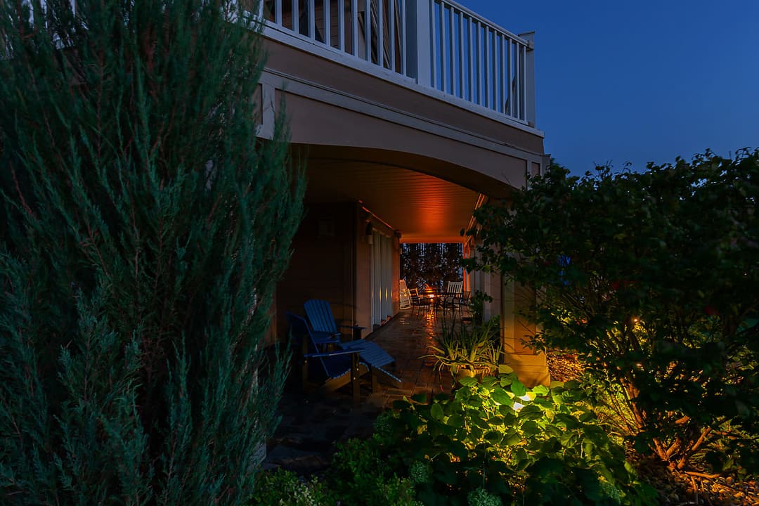 Cozy outdoor patio with blue chairs and soft lighting at dusk surrounded by greenery.