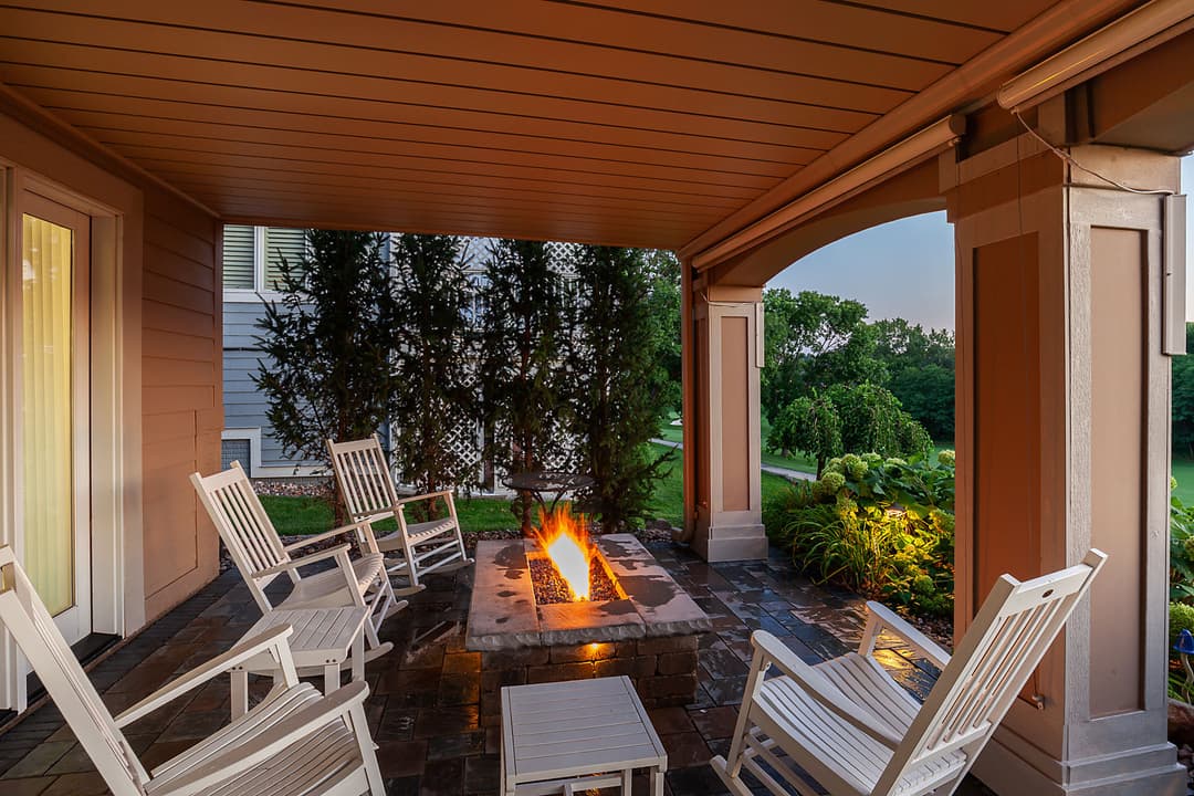 Cozy outdoor seating area with rocking chairs and a fire pit surrounded by greenery.
