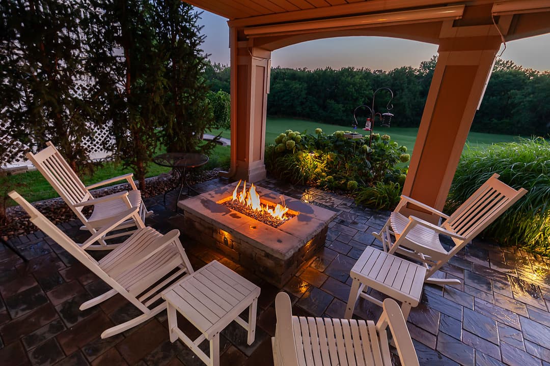 Cozy outdoor fire pit surrounded by white chairs in a scenic garden setting.