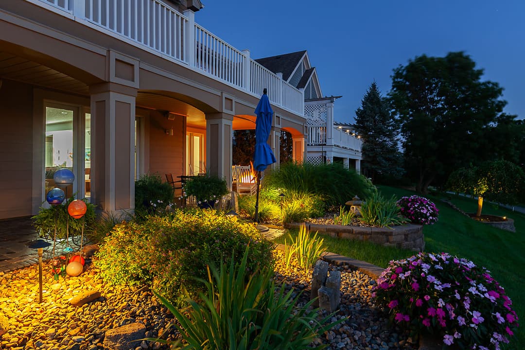 Elegant backyard at dusk with lush landscaping, flower beds, and soft garden lighting.