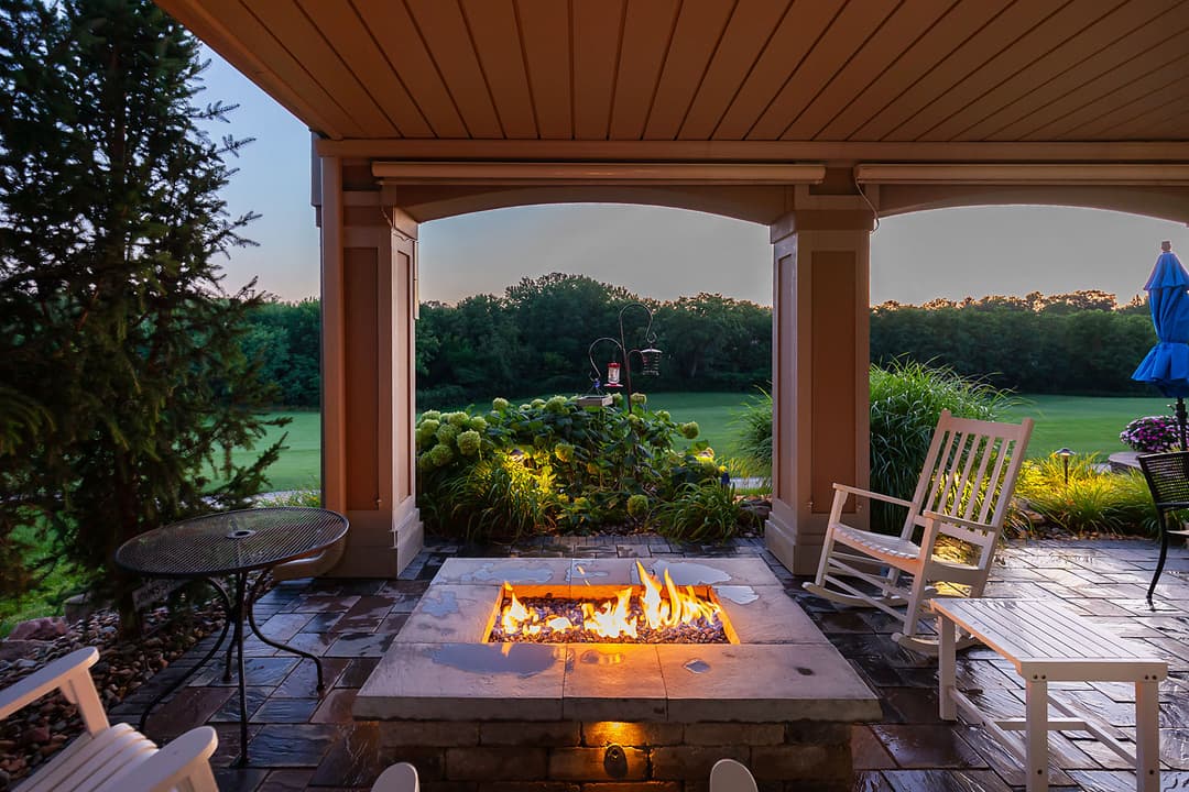 Cozy patio with a fire pit, rocking chairs, and lush greenery at sunset. Relaxing outdoor space.