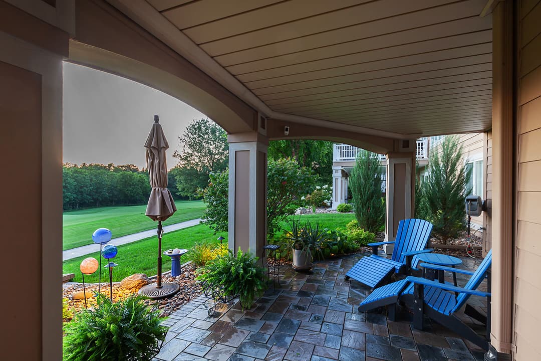 Cozy patio with blue chairs, umbrella, and vibrant garden overlooking a lawn at sunset.