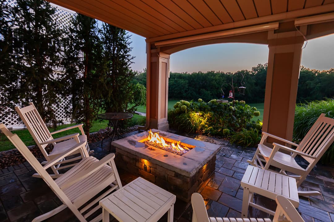 Cozy outdoor seating area with a fire pit surrounded by greenery at dusk.