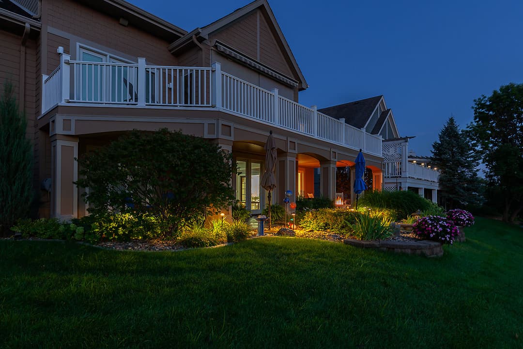 Elegant outdoor patio with illuminated landscaping at dusk, showcasing vibrant flowers and greenery.