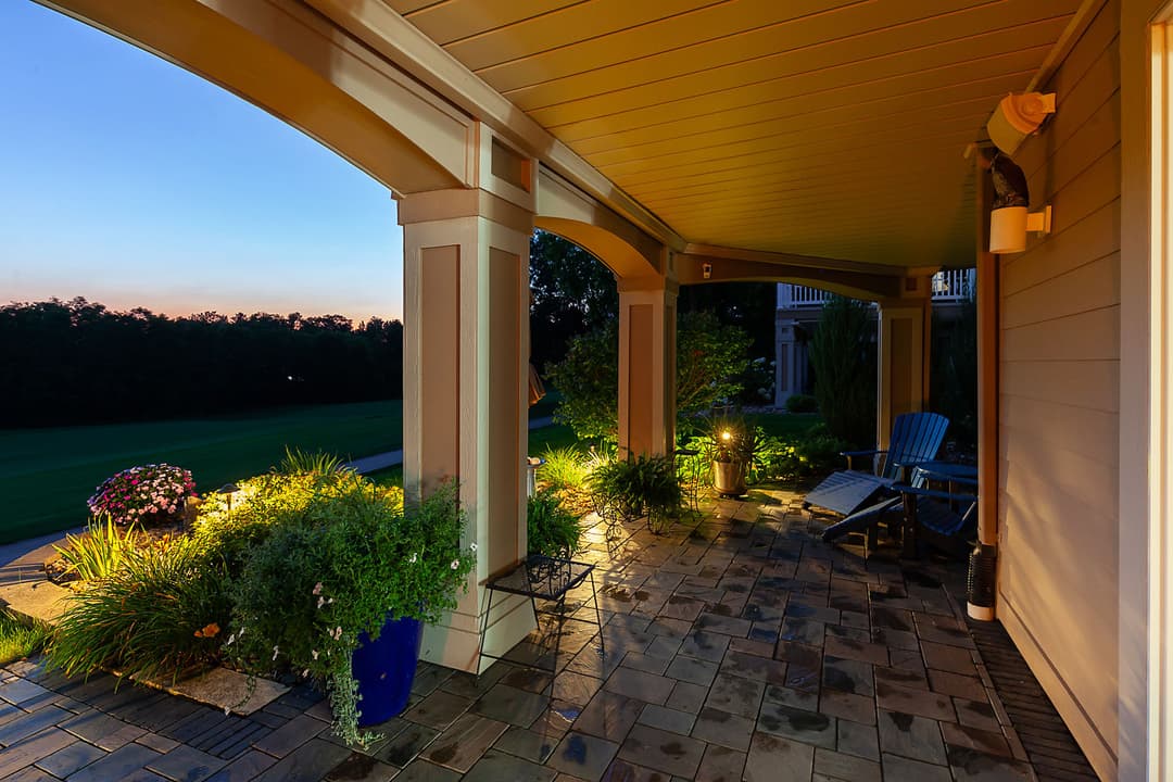Welcoming porch at dusk with lush plants, blue chairs, and warm lighting.