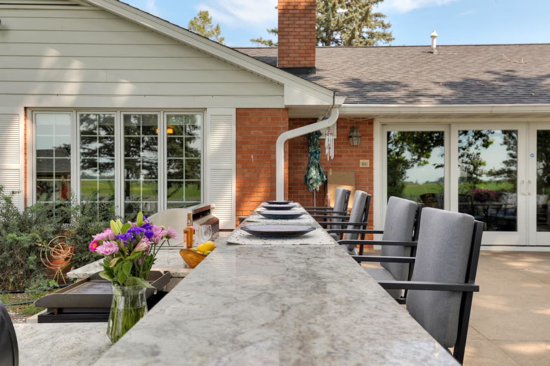 Outdoor dining area featuring granite countertop, bar stools, and flower vase with colorful blooms.