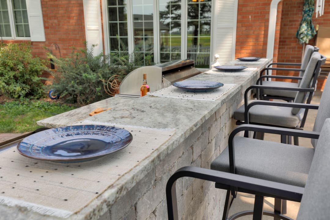 Outdoor dining setup with elegant plates and bar stools beside a stone countertop.