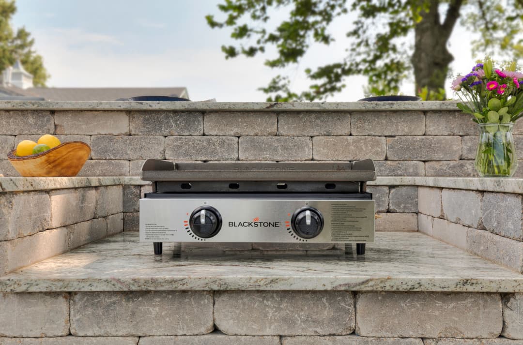 Blackstone griddle on outdoor stone steps with flowers and fruit bowl in background.