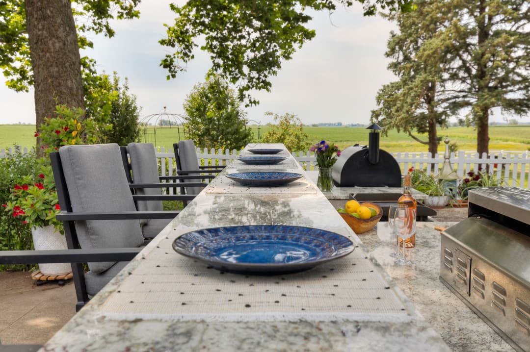 Outdoor dining area with blue plates, grill, and scenic views of greenery and trees.