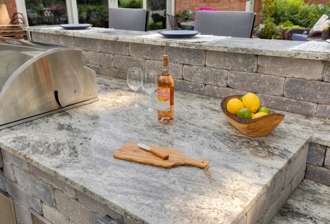 Outdoor kitchen with granite countertop, wine, glasses, and a fruit bowl. Perfect for gatherings.