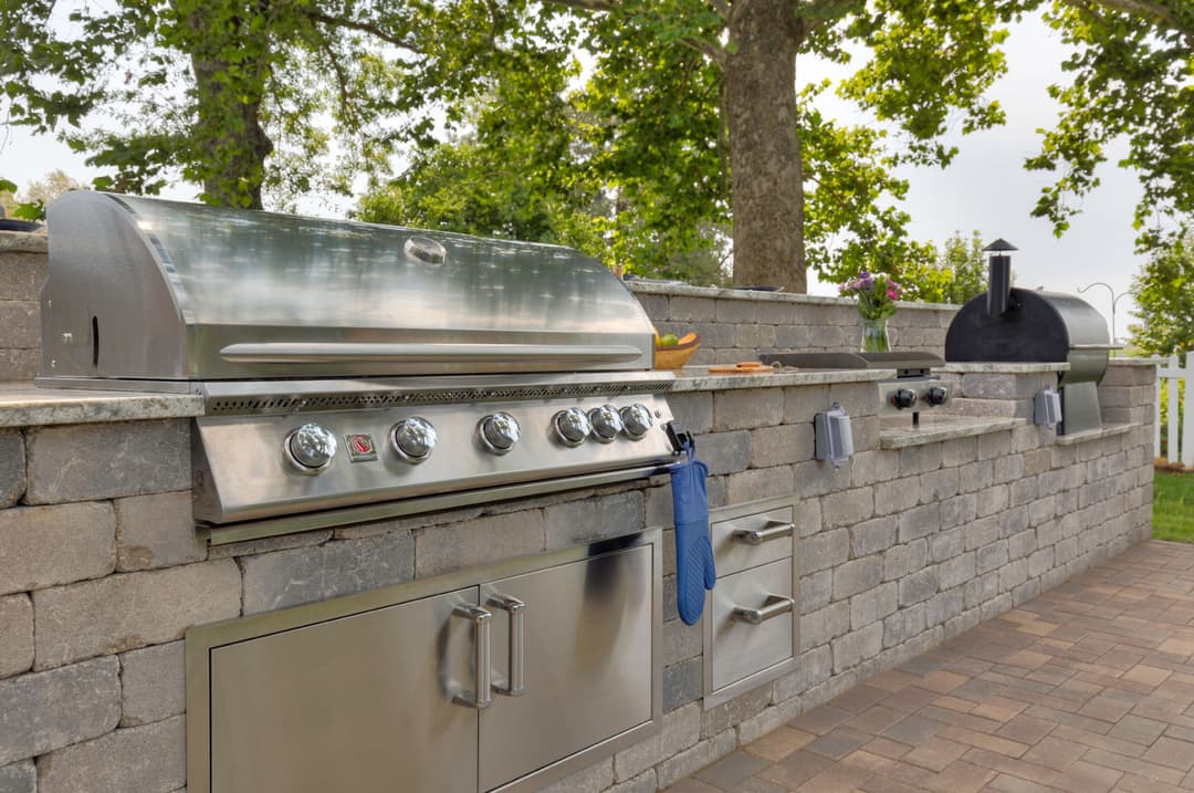 Stainless steel outdoor grill on a stone patio with trees in the background.