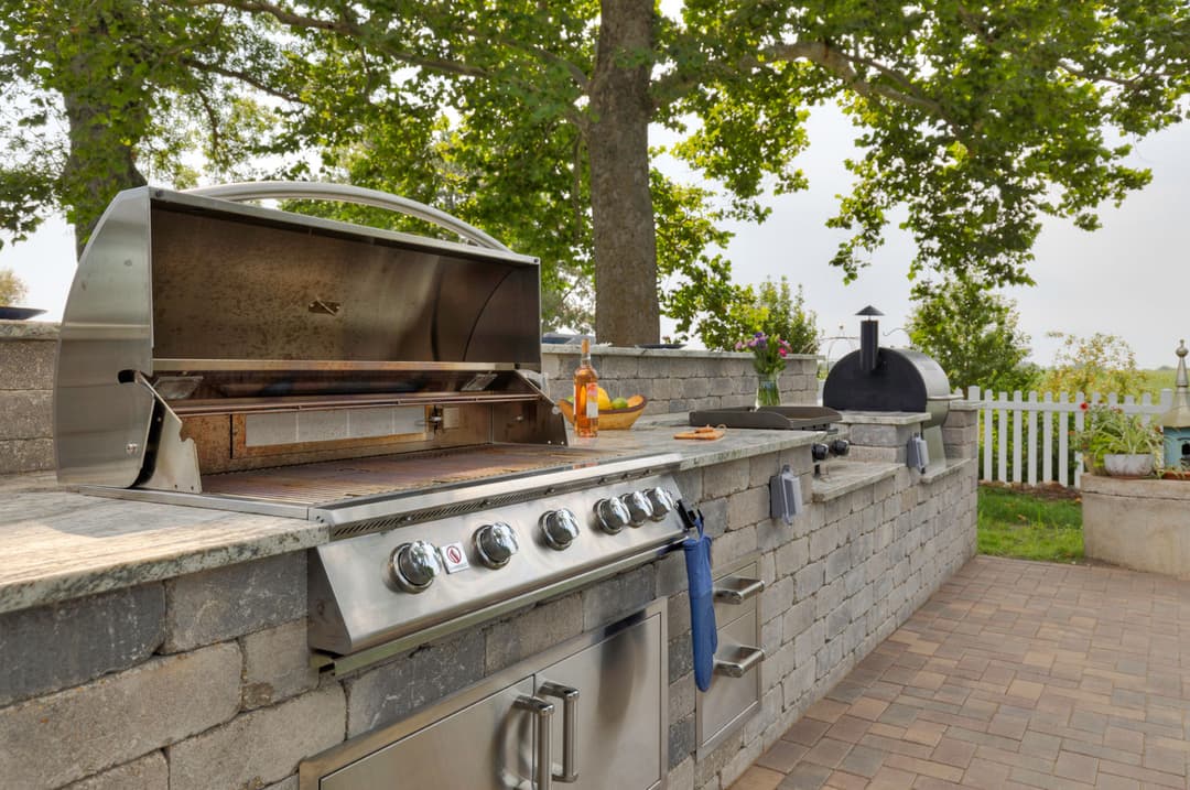 Modern outdoor kitchen with stainless steel grill, stone countertop, and scenic view.
