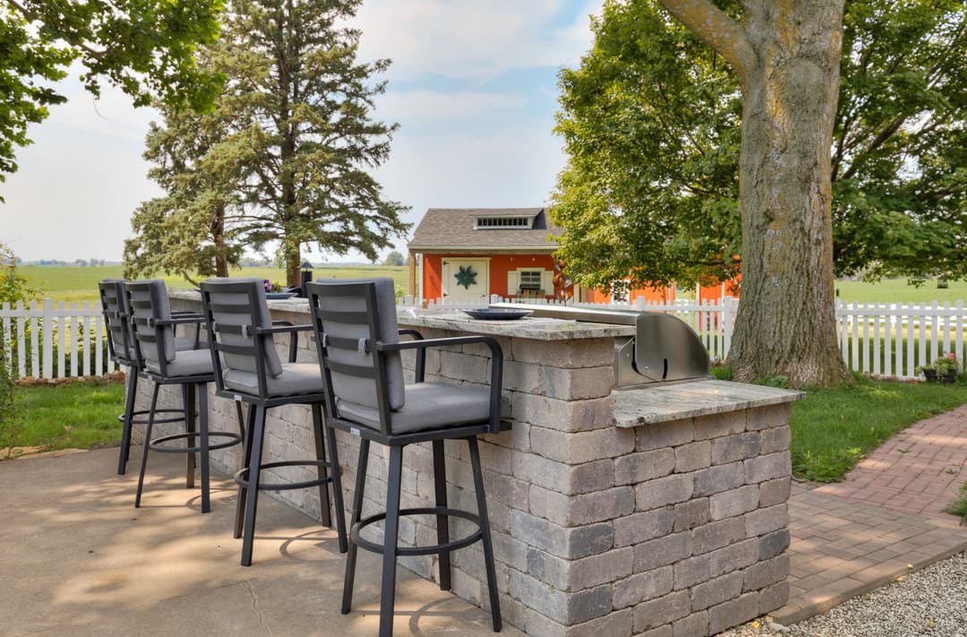 Outdoor bar with high chairs overlooking a scenic backyard and garden shed.